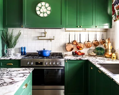 A colourful cottage-style kitchen with green cupboards and a marble island.