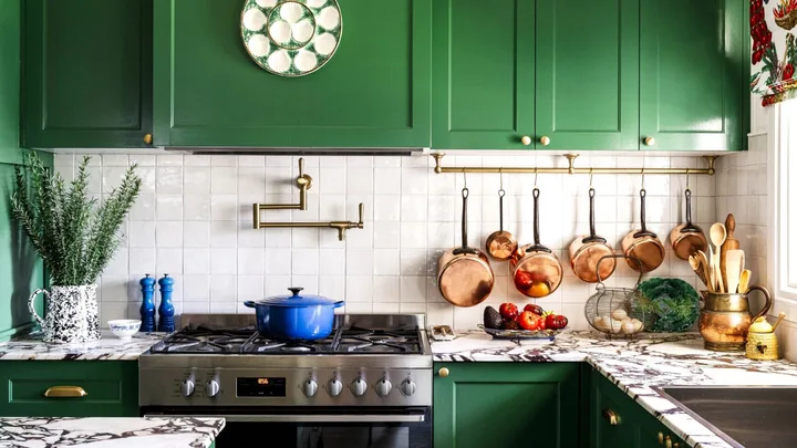 A colourful cottage-style kitchen with green cupboards and a marble island.