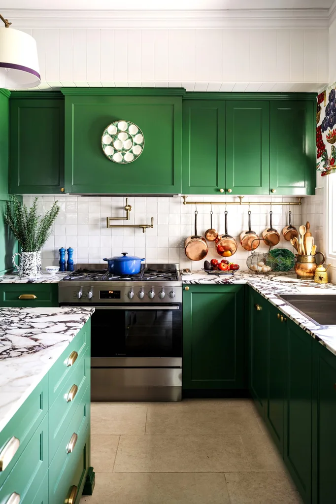 A colourful cottage-style kitchen with green cupboards and a marble island.