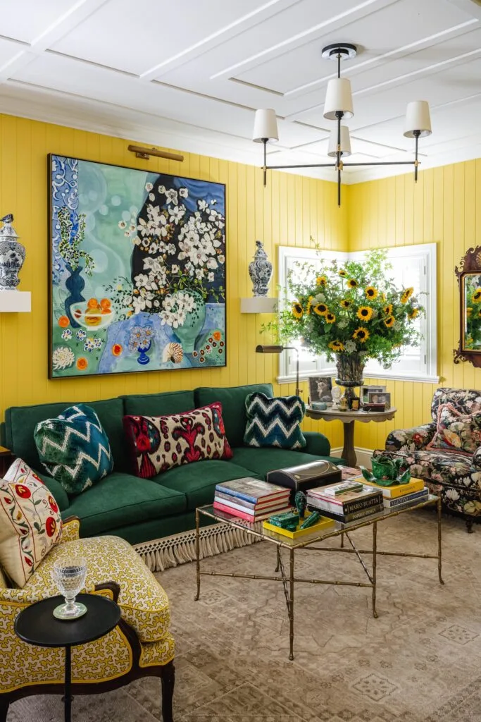 A bright yellow living room with a green sofa and large floral artwork.