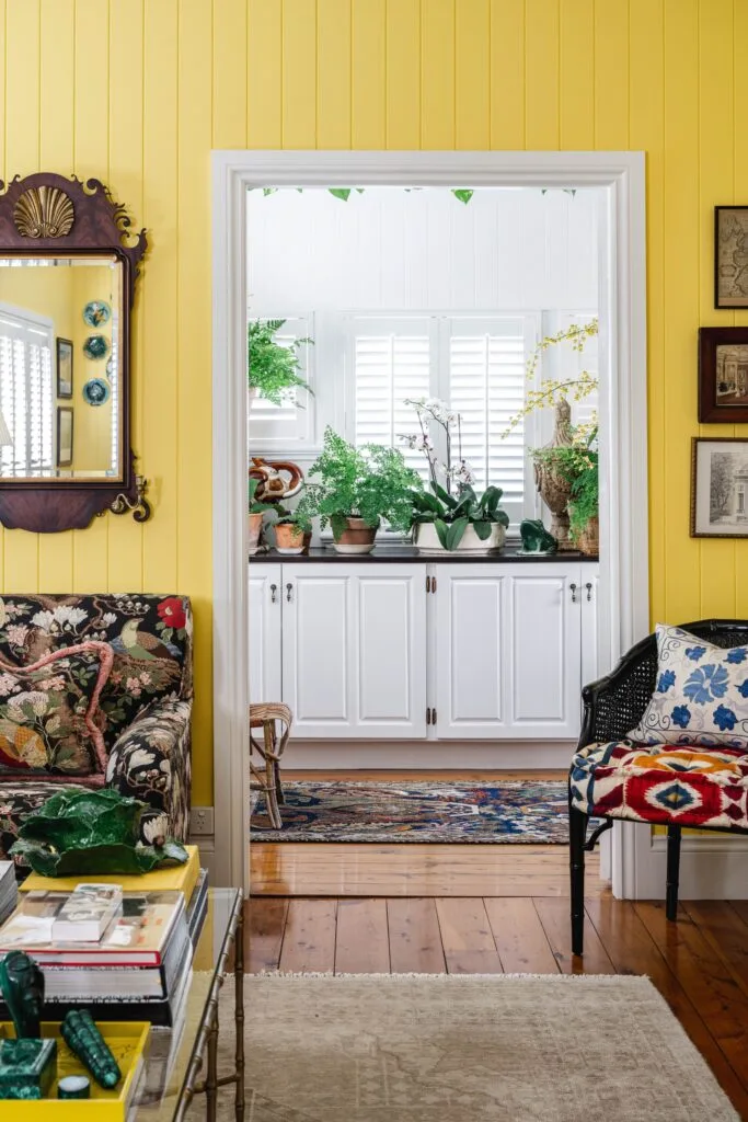 A bright yellow living room looking into a kitchen with white cabinets.