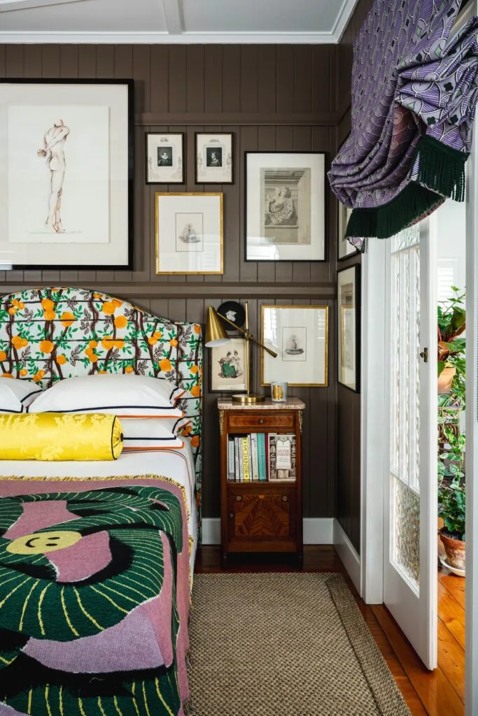 A bright main bedroom with an orange printed bedhead, purple curtains and brown panel walls.