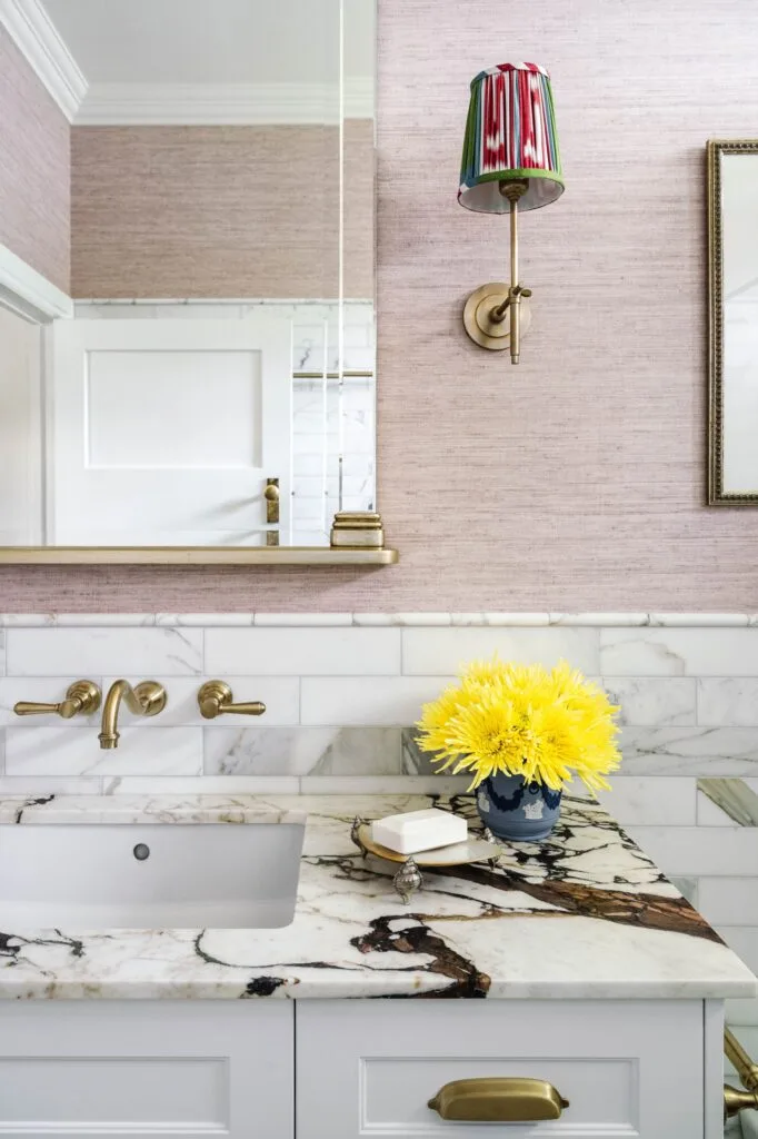 A marble vanity with matching tiled walls and a vintage style mirror.