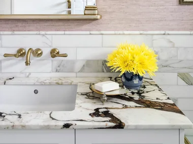 A marble vanity with matching tiled walls and a vintage style mirror.