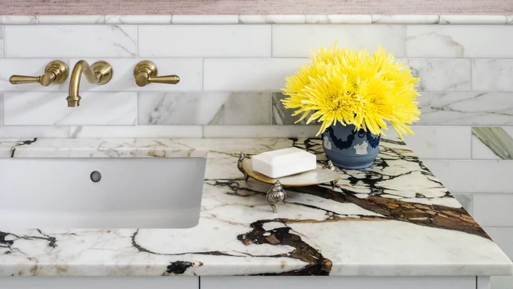 A marble vanity with matching tiled walls and a vintage style mirror.