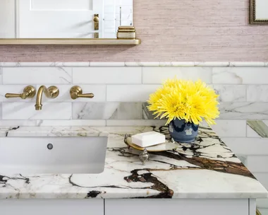 A marble vanity with matching tiled walls and a vintage style mirror.