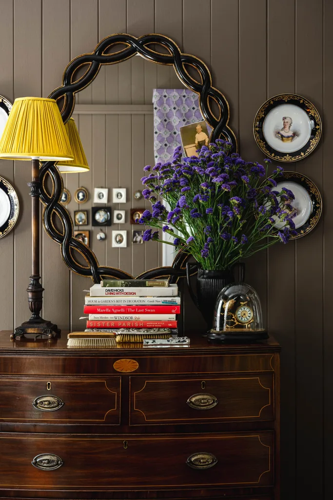 A vintage style dressing table with a lamp and purple flowers.