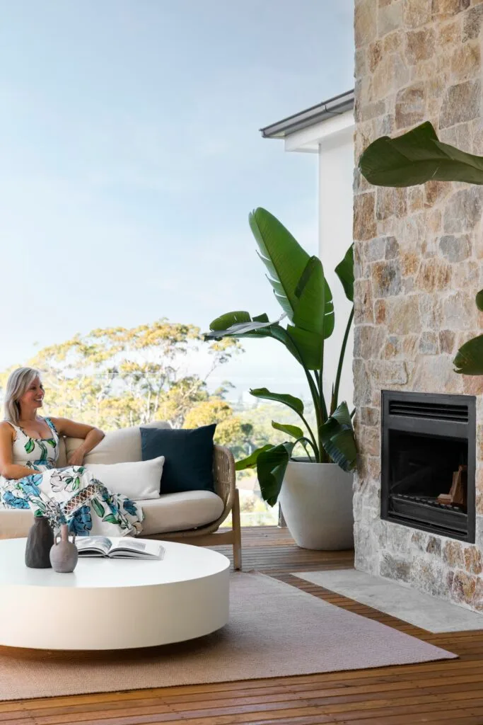 Lisa sitting in the outdoor alfresco area by a stone fireplace.