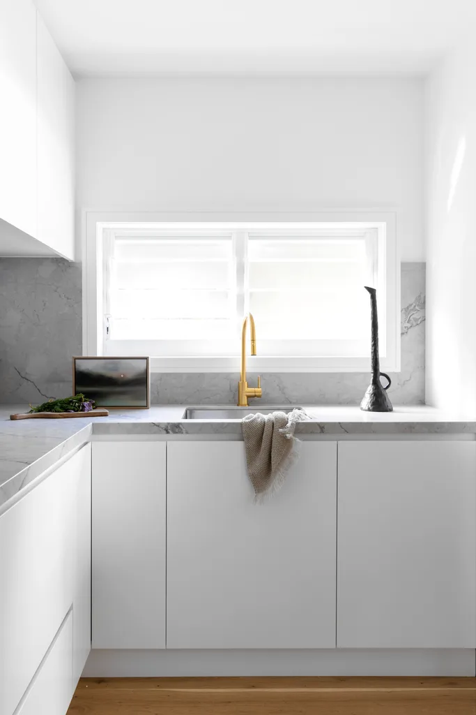 A white and grey marble butler's pantry with gold tapware.