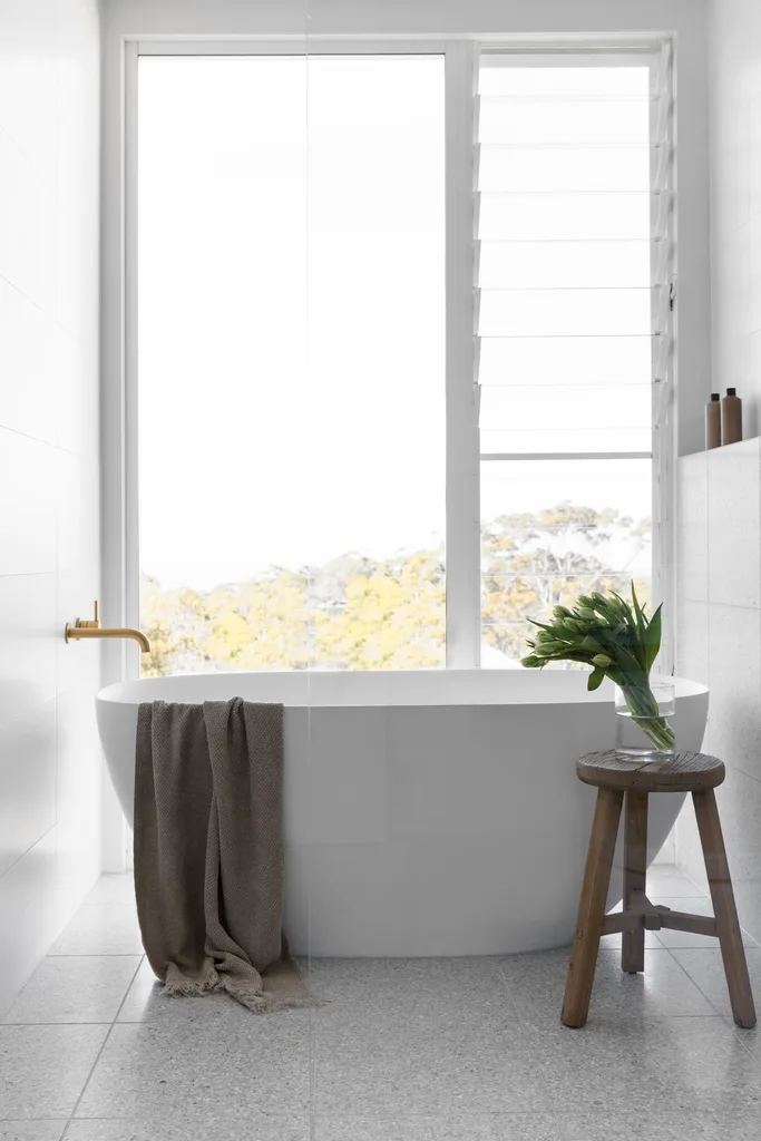 A white coastal ensuite with a freestanding bath and floor to ceiling window.