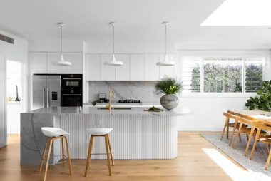 A white coastal-style kitchen with a fluted island and grey marble.