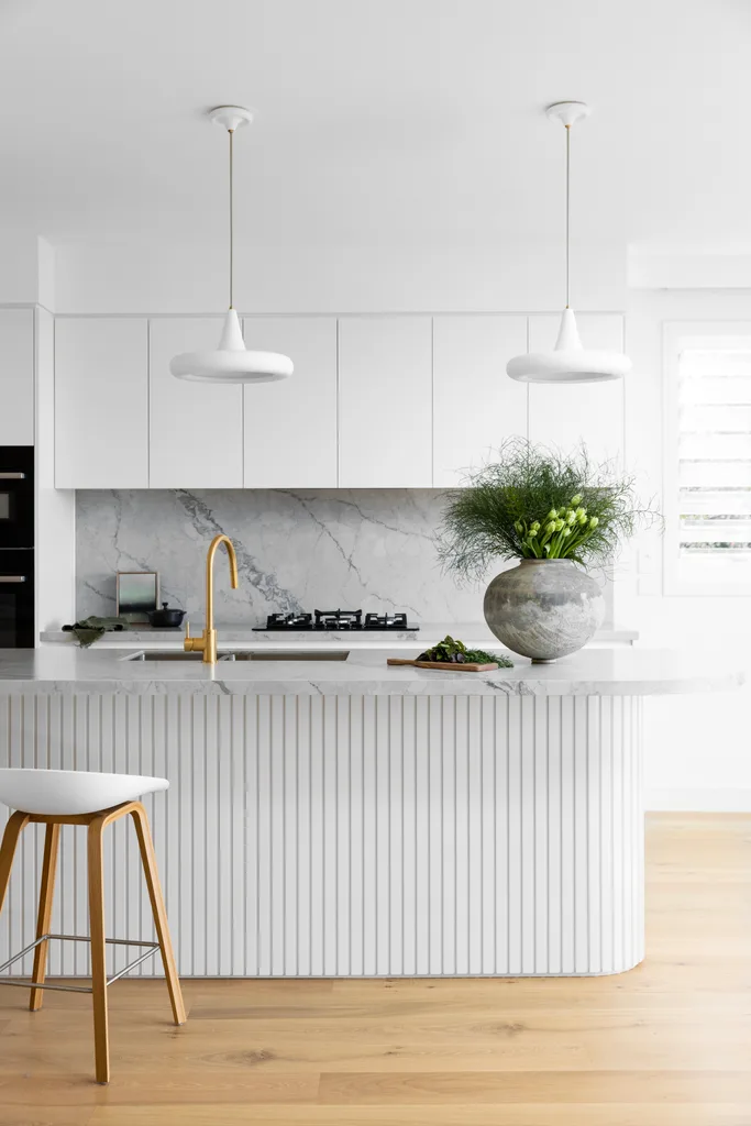 A fluted kitchen island with gold tapware and round hanging pendant lights.