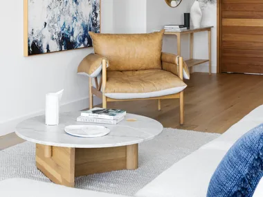 A white living area with a tan leather chair beside an abstract artwork.