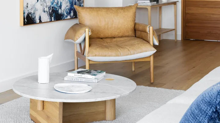 A white living area with a tan leather chair beside an abstract artwork.