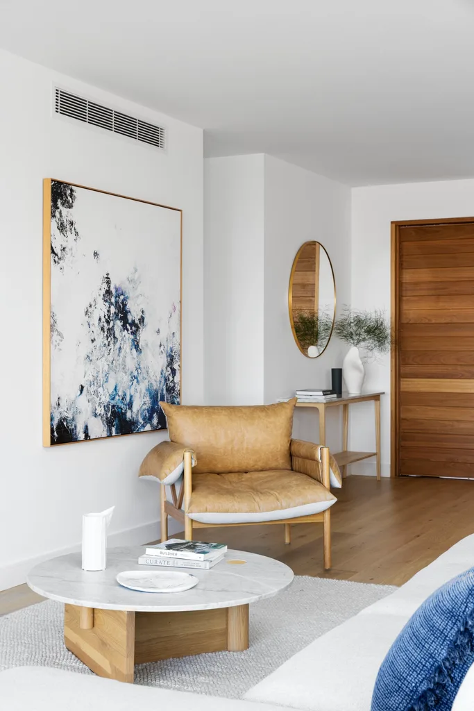 A white living area with a tan leather chair beside an abstract artwork.