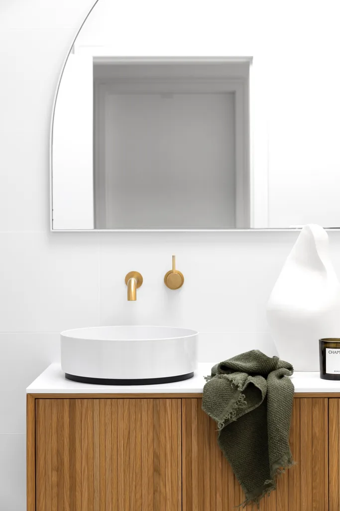 A timber vanity with a counter basin and arched mirror.