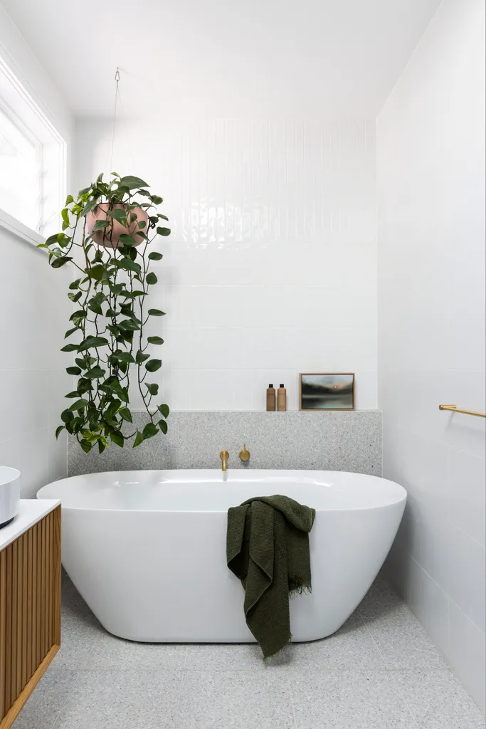 A white and grey tiled bathroom with a freestanding bath and hanging plant.