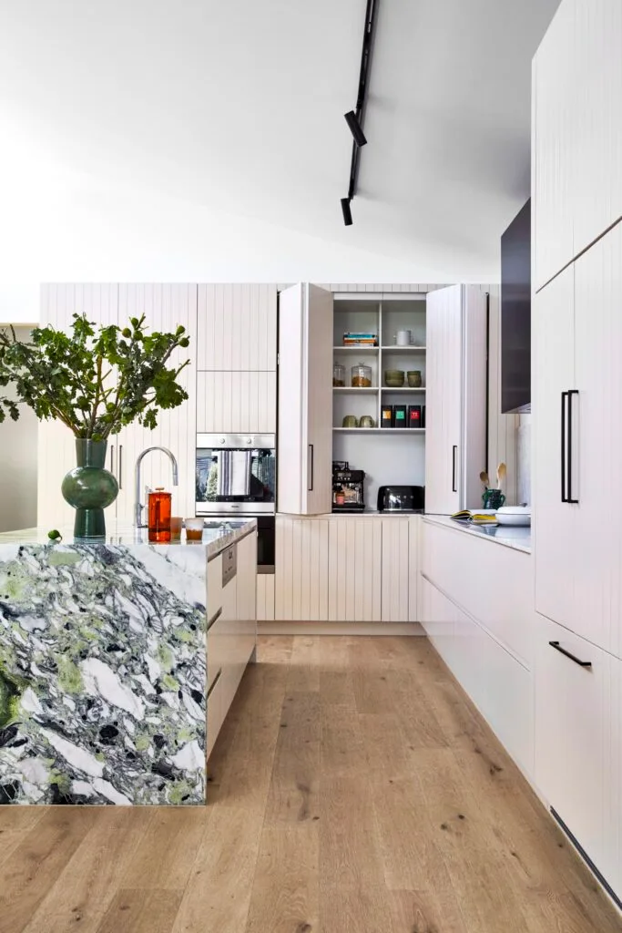 A kitchen with a marble island and white panelled retractable cupboard doors.