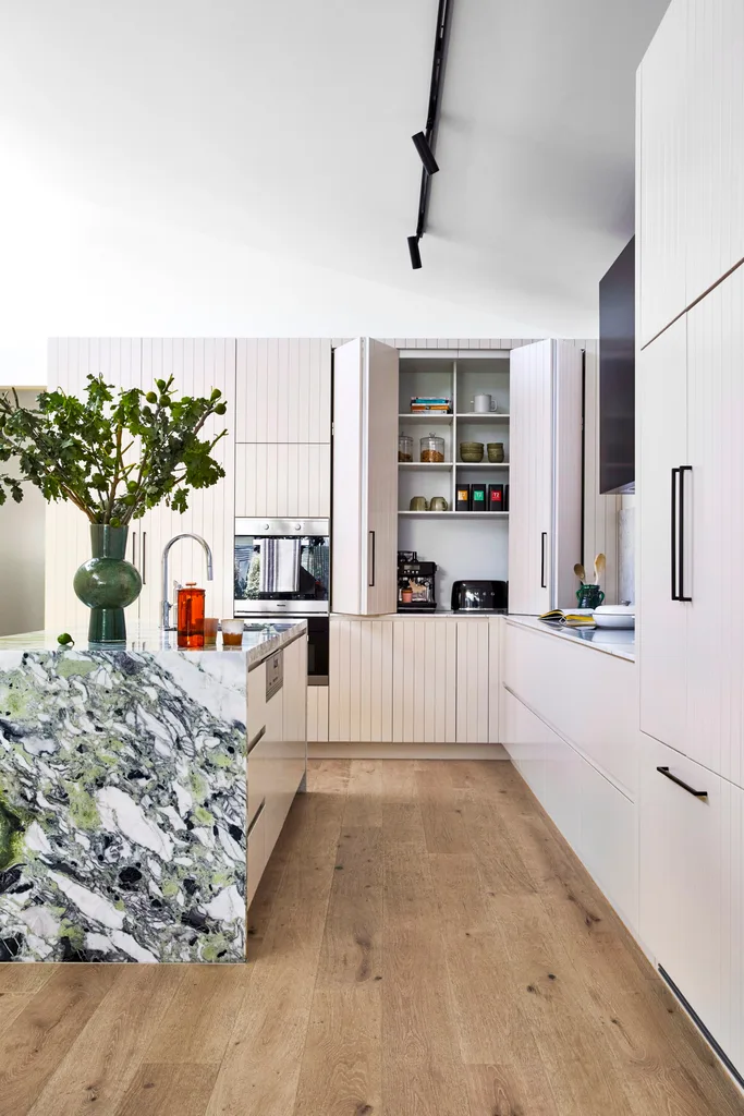 A kitchen with a marble island and white panelled retractable cupboard doors.
