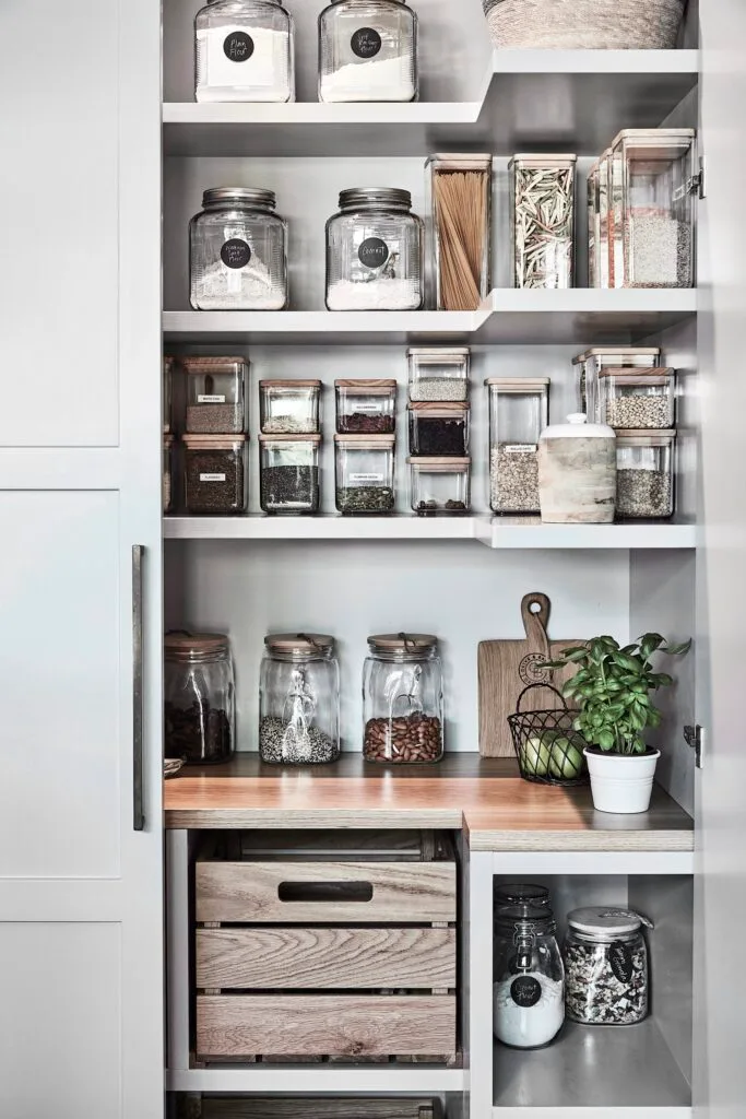 Open pantry shelving with a timber bench and glass storage containers.