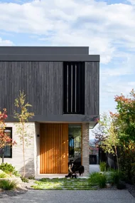 A modern minimalist house with stone and black cladding and two border collies beneath.
