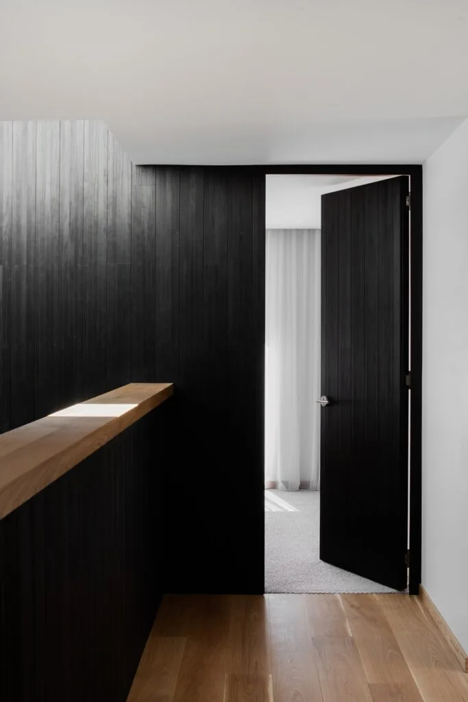 A landing and open door in black timber cladding.