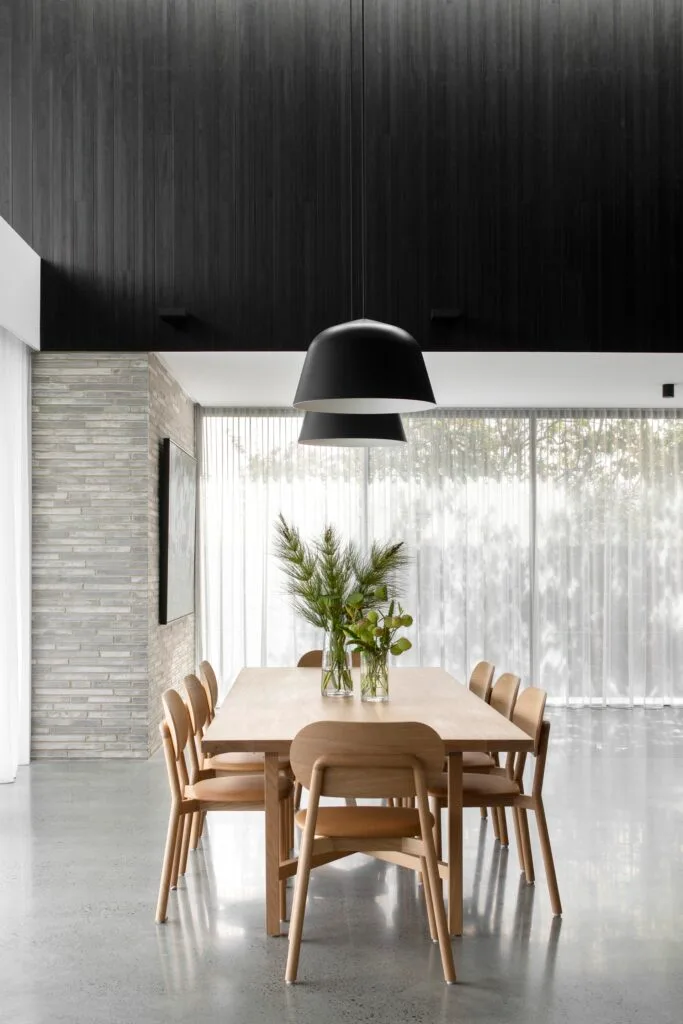 A minimalist black and grey dining room with a timber table and round hanging pendants.