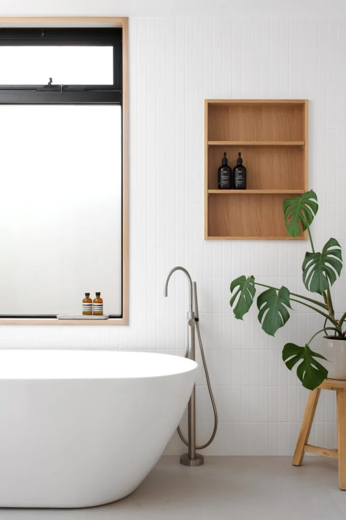 A minimalist all-white bathroom with a freestanding bath and timber shelves.