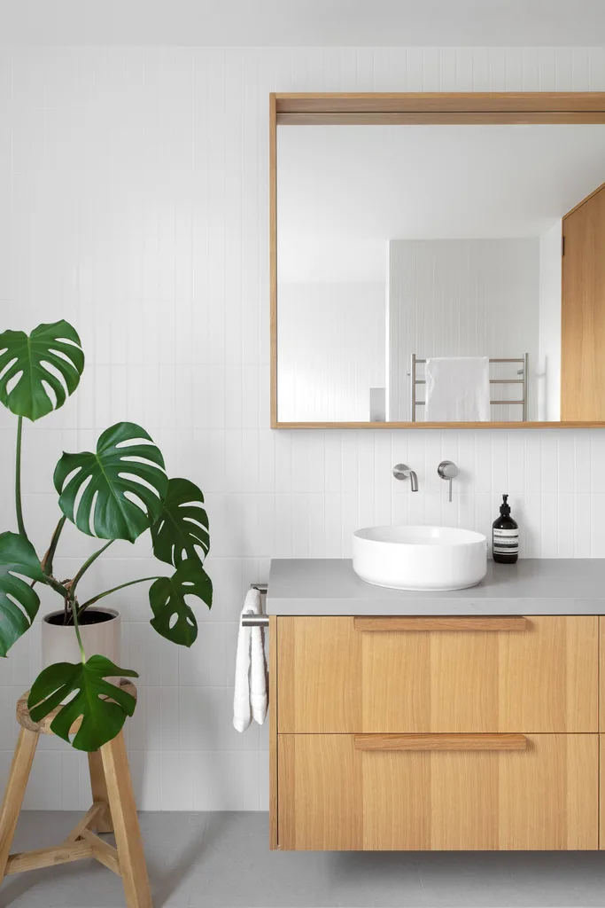 A minimalist bathroom with a timber vanity, mirror and monstera plant.