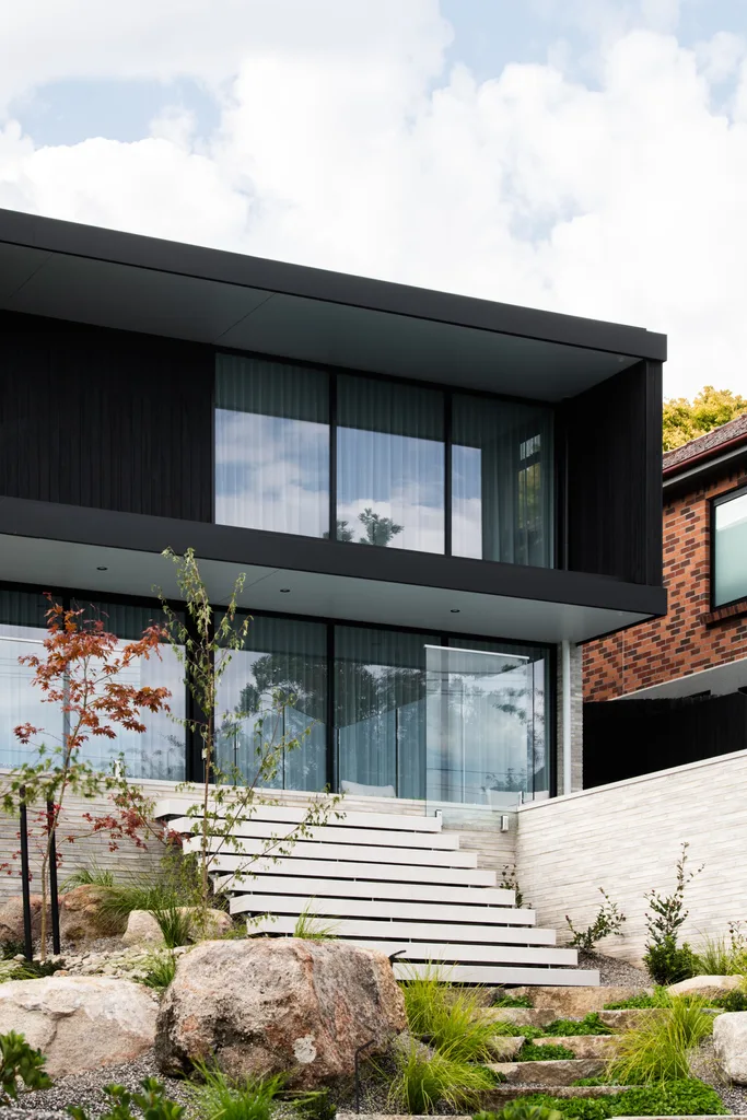 Steps leading to a rectangular minimalist home with black cladding and expansive windows.