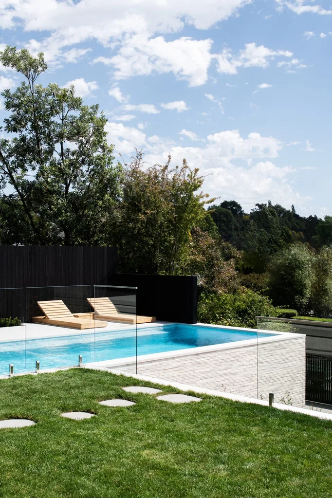 A white extended pool with timber loungers and a glass fence. backyard pool ideas