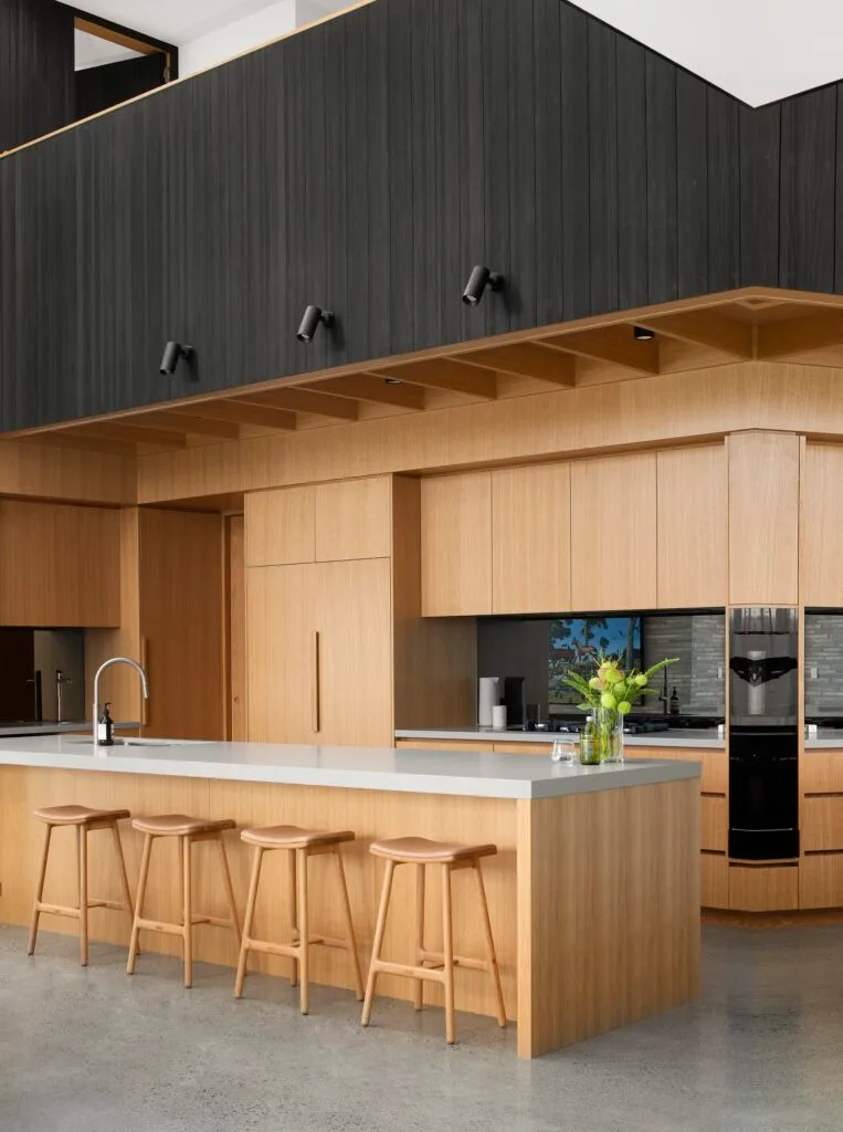 A minimalist timber and black cladded kitchen with a grey topped island.