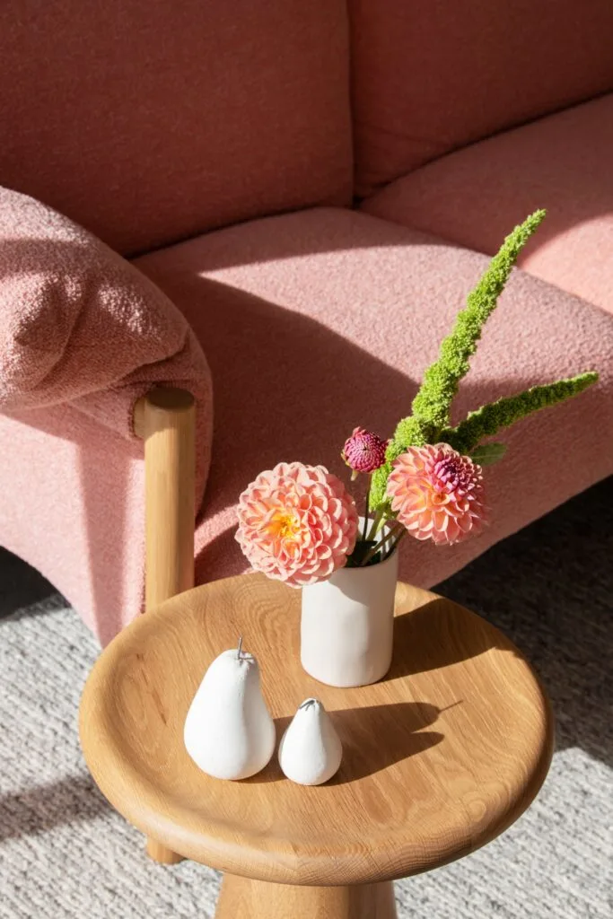 A round side table with a vase of pink flowers.