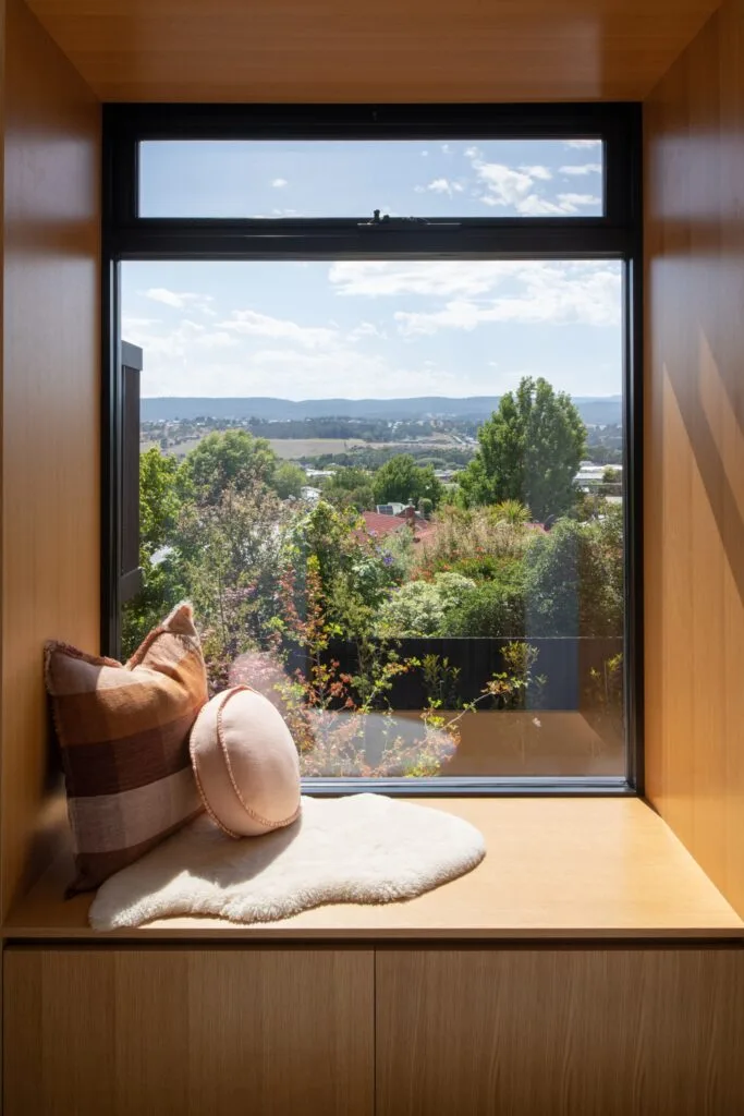 A timber window seat with a view of trees and mountains.