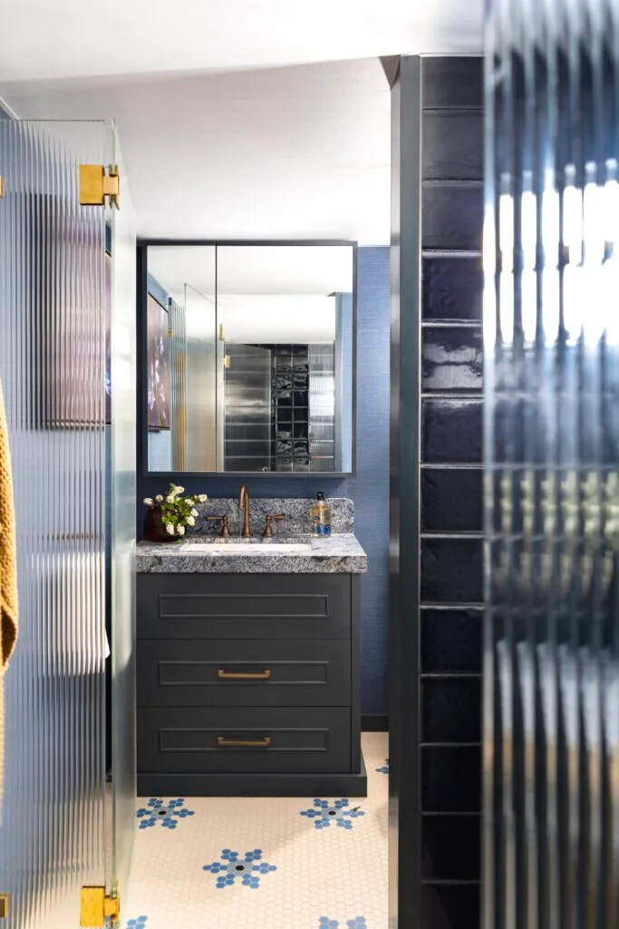 A moody navy bathroom with snowflake mosaic floors, a stone-topped vanity and fluted glass.