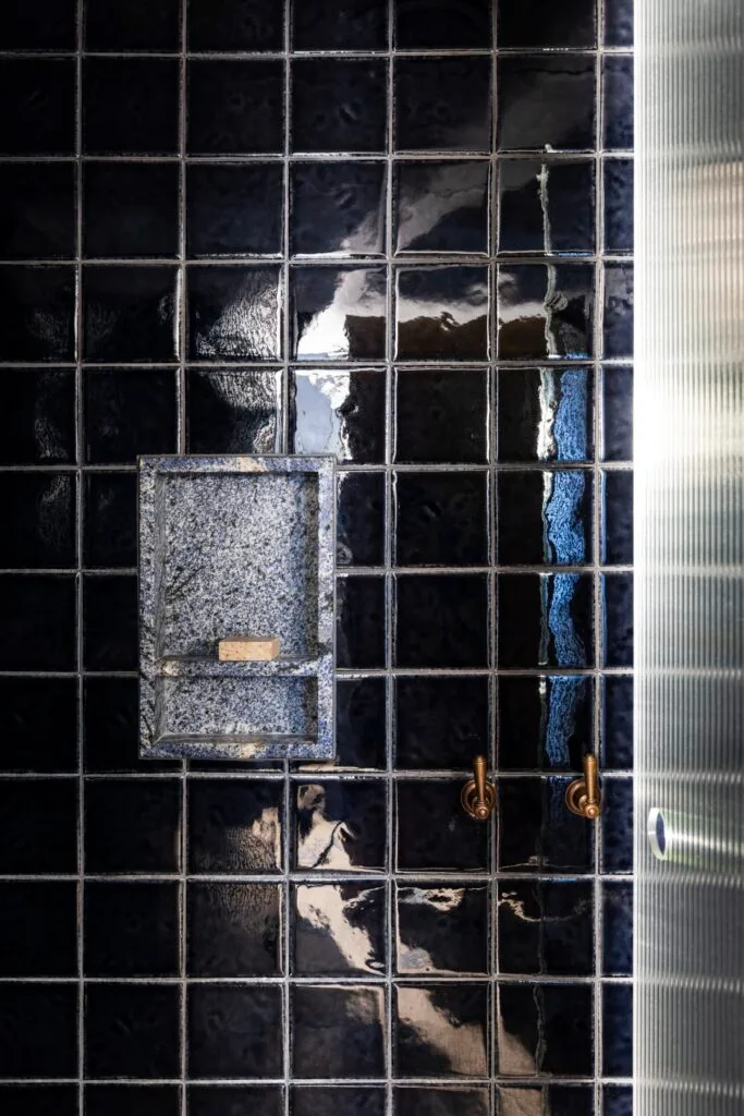 A black-tiled shower with bronze tapware by a shower niche.