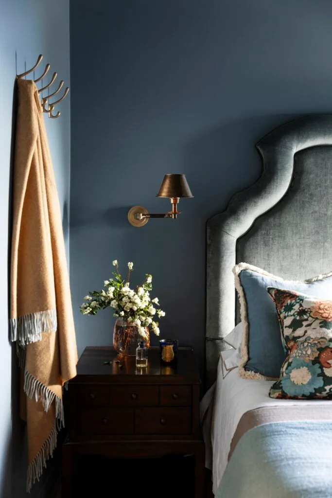 A moody blue bedroom with a soft blue bedhead, side table and coat hooks.