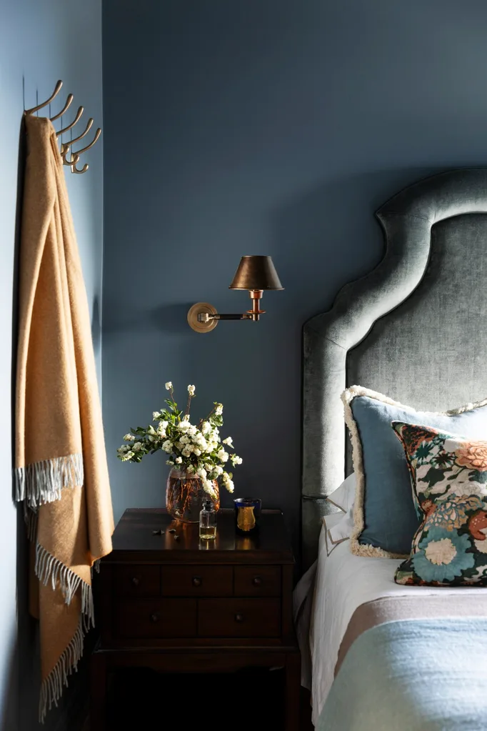 A moody blue bedroom with a soft blue bedhead, side table and coat hooks.