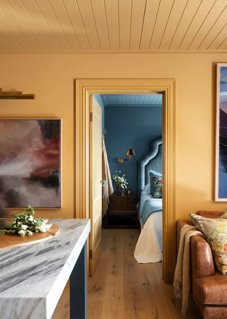 A mustard yellow living room with a leather sofa and marble table.