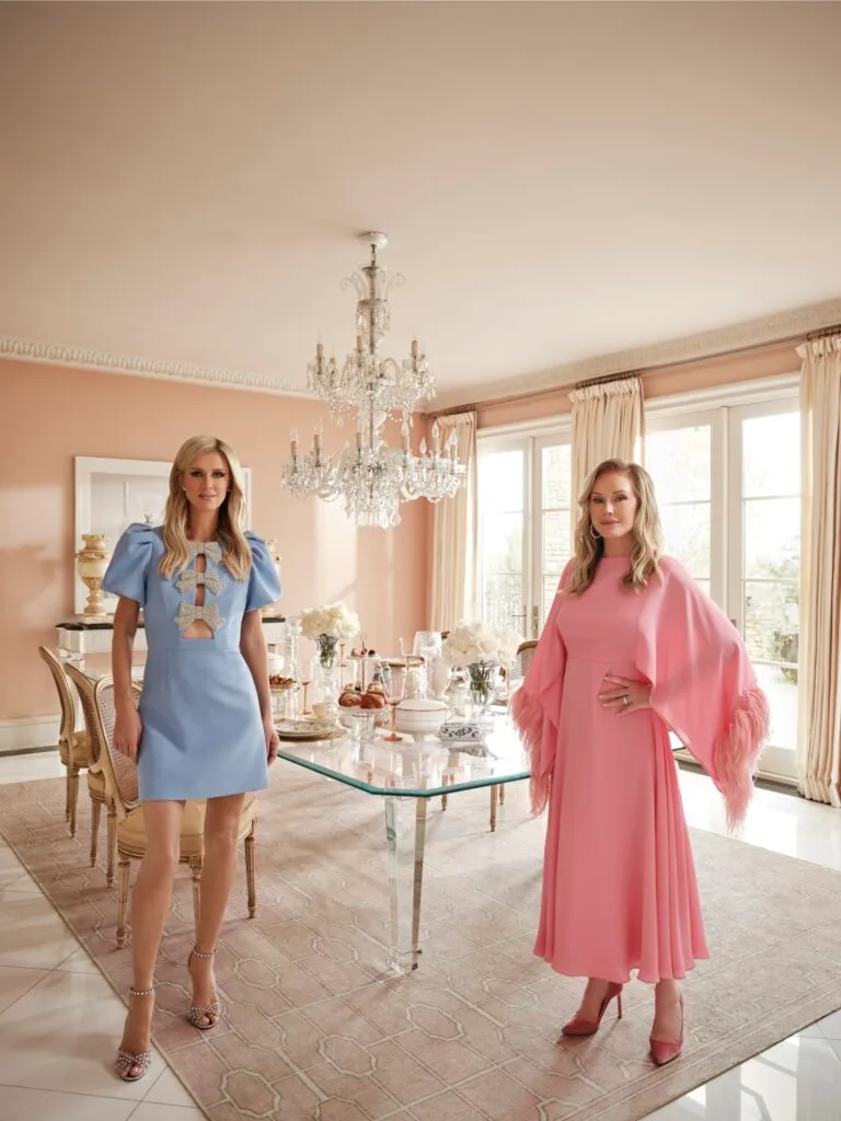 Nicky and Kathy Hilton stand next to a glass dining table on a very pale creamy pink Ruggable rug