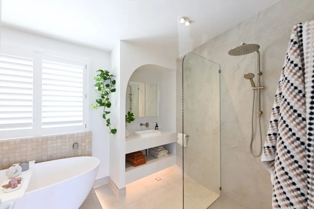 Rhys and Liam's Dream Home bathroom with a bathtub on a floating platform, sink in a built-in arch and simple shower with glass partition next to it.