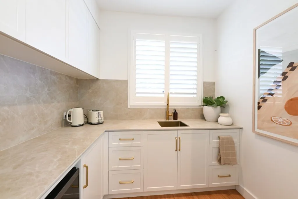 Rhys and Liam's Dream Home butler's pantry with natural coloured bench that's continued up the splashback and white cabinetry with gold handles.