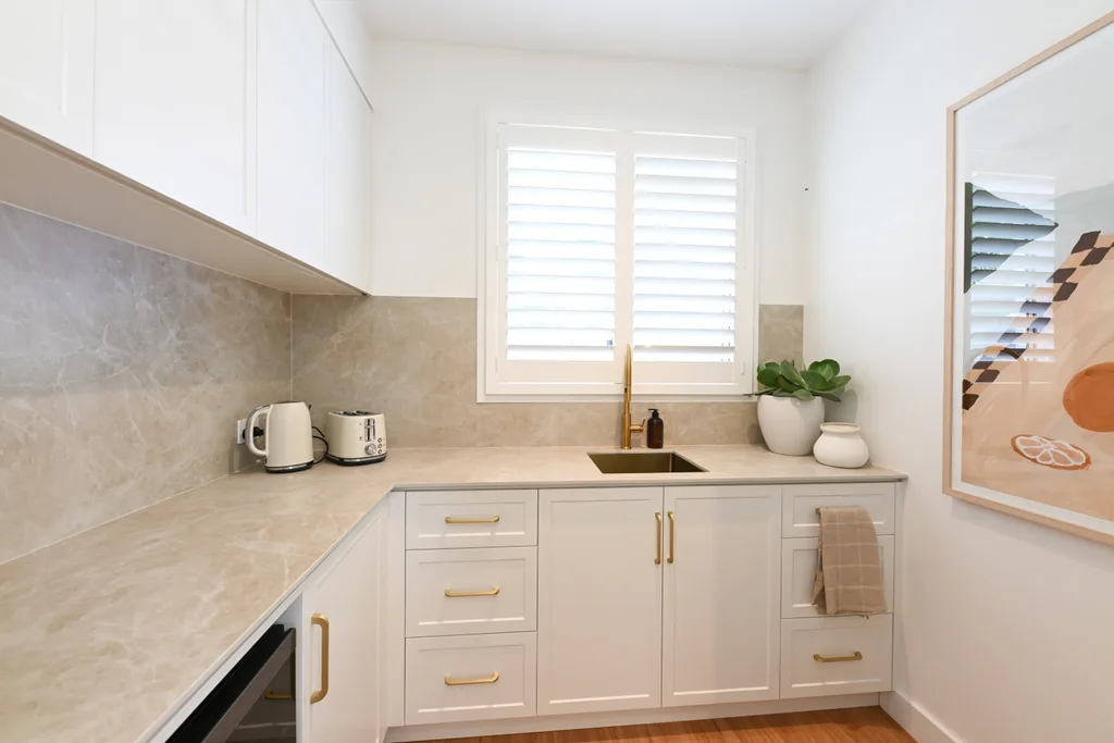 Rhys and Liam's Dream Home butler's pantry with natural coloured bench that's continued up the splashback and white cabinetry with gold handles.