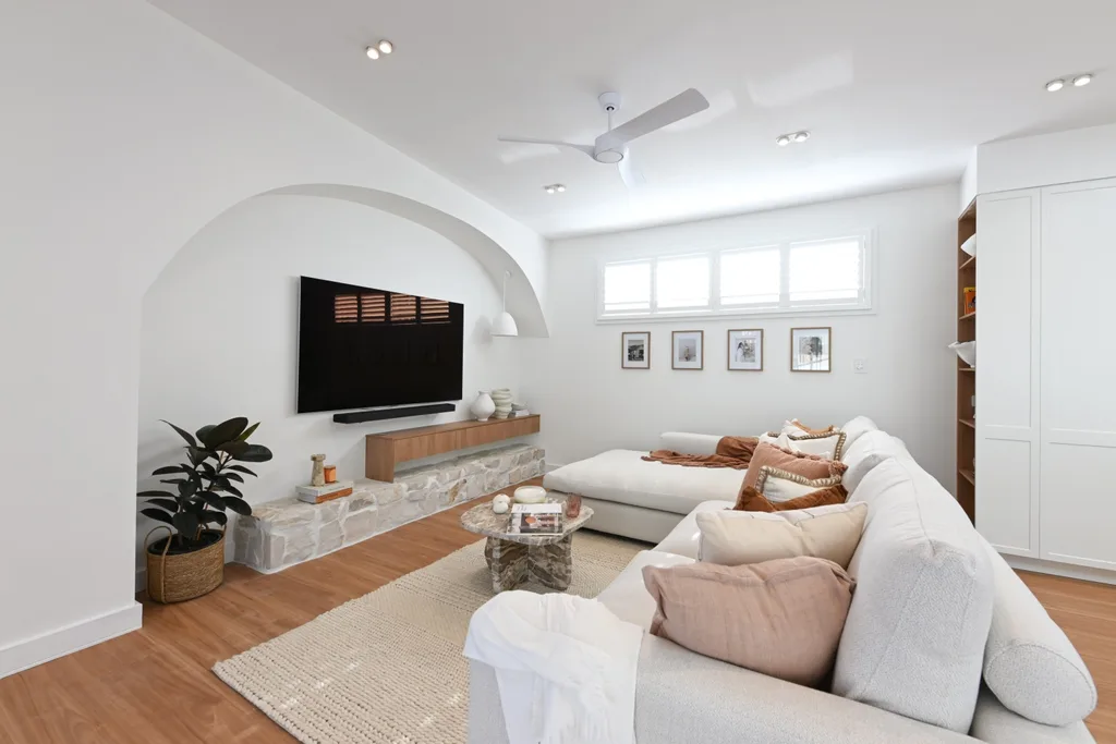 Rhys and Liam's Dream Home living room with a white couch and array of cushions in pale pink and terracotta with a TV in an arch.