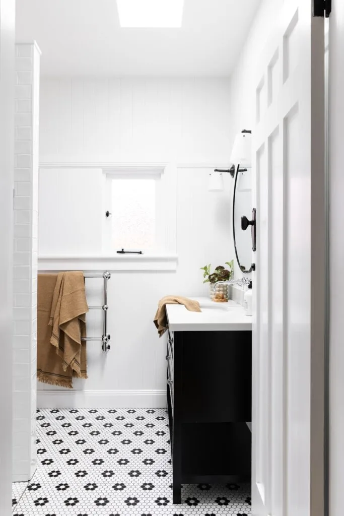 A bright white bathroom with black and white mosaic tiles and vanity.