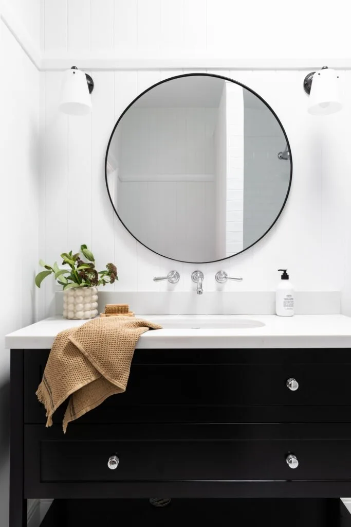 A black and white vanity with a circle mirror above.