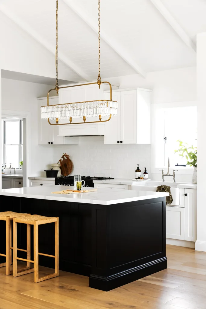 A white and black Hamptons style kitchen with a chandelier over an island.