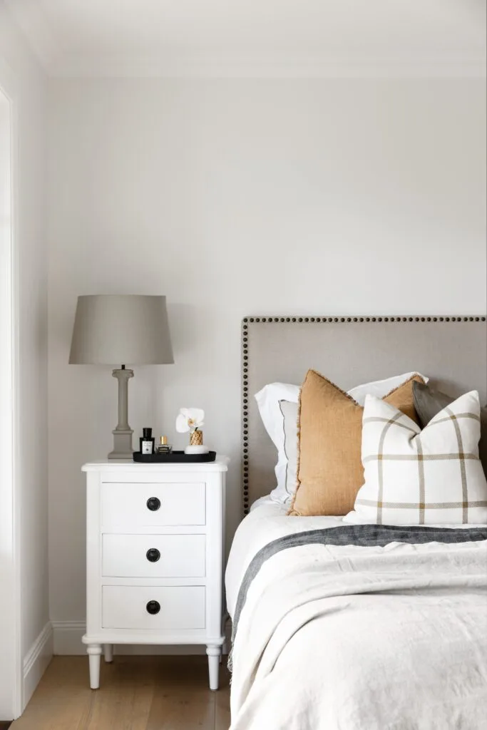 A white bedroom with a beige bedhead and white side table.