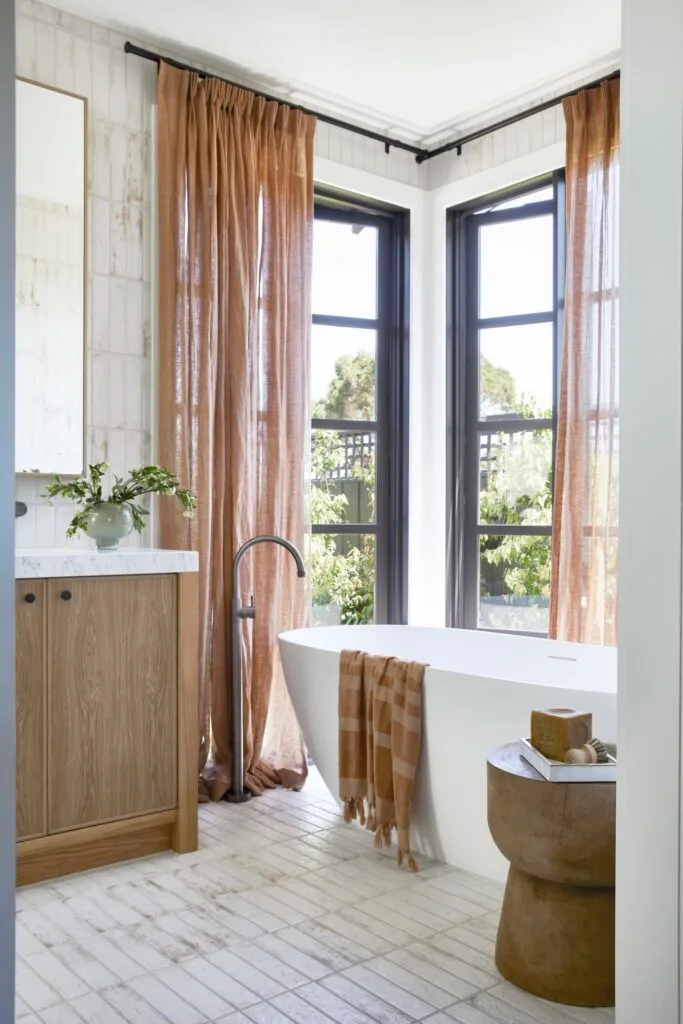 A freestanding bath surrounded by windows and blush curtains.