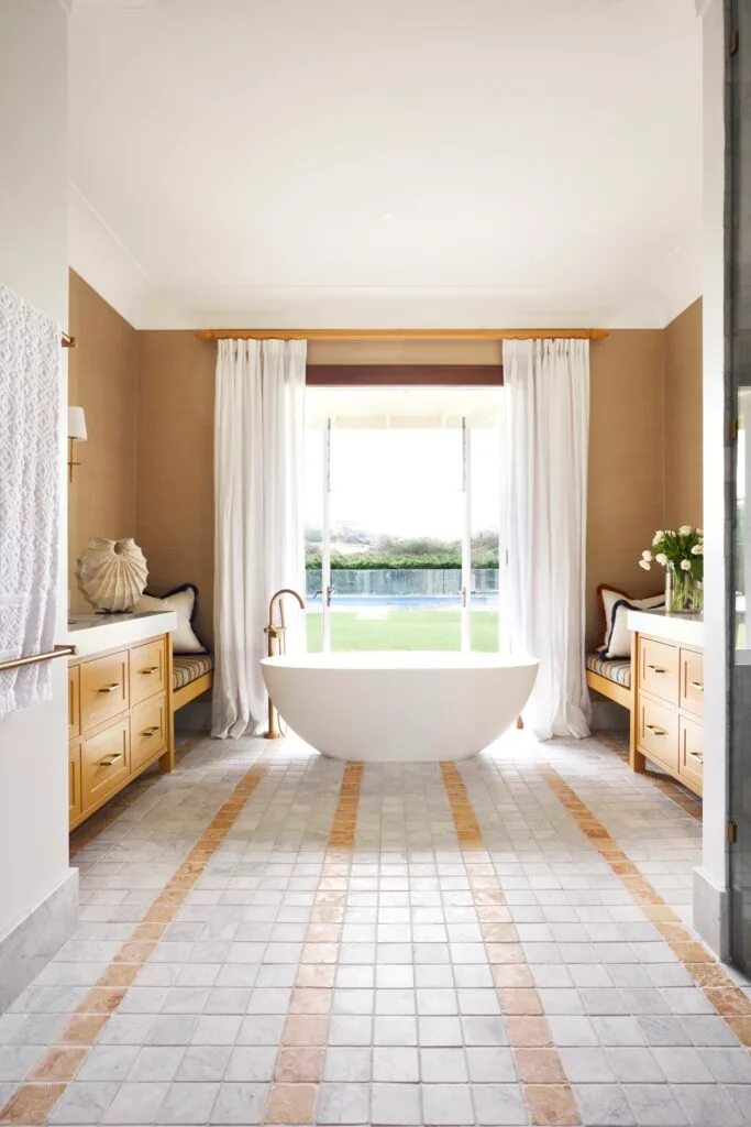 Tumbled stone tiles leading to a freestanding bath by a window.